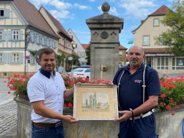 Georg Geheeb übergibt Zweiter Bürgermeister Thomas Wagenhäuser das besondere Gemälde in Hofheim i. UFr. auf dem Marktplatz. (Foto: Georg Metzger)