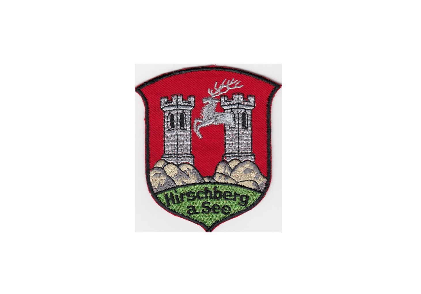 Stadtwappen von Hirschberg (Doksy), Abb. zwei Türme auf roten Untergrund, darunter steht Hirschberg a. See auf grünem Untergrund.